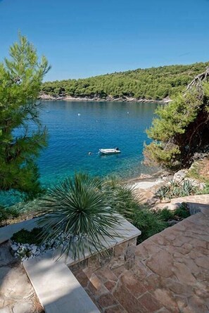 A coastal view with a boat on the water, surrounded by greenery and a stone pathway.