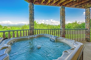 Un jacuzzi bajo un pérgola de piedra con vistas a árboles verdes y montañas.
