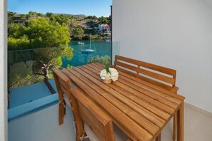 A wooden table with a bench on a balcony overlooking a bay with boats and houses.