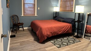 Ein Schlafzimmer mit einem Bett, zwei Nachttischlampen, einem Sessel, einem Fenster und einem Spiegel.