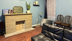 Ein Wohnzimmer mit Kamin aus Stein, einer Couch, einer Zimmerpflanze und einem Bücherregal.