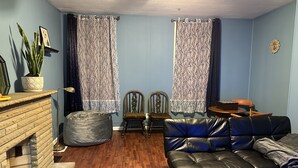 Ein Wohnzimmer mit Kamin, einem schwarzen Ledersofa, zwei Holzstühlen, einem Couchtisch und einem Blumentopf.