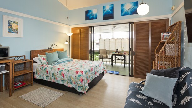 A bedroom with a bed, a desk, a chair, a sofa, and a balcony with a table and chairs. - Happy Honu Oasis, Surf shack with pool and A/C (Hilo)