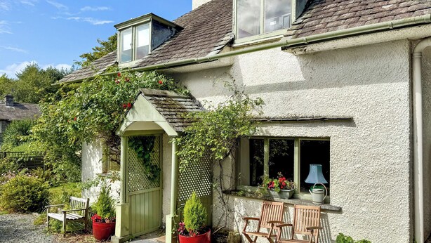 A quaint house with a sloped roof, a small porch with a green door, and a window with a white frame. - 2 bedroom accommodation in Sawrey, near Ambleside (Sawrey, near Ambleside)