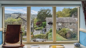 A window with a view of a stone house, a wooden chair, a small plate, and a tray on the windowsill. - 2 bedroom accommodation in Sawrey, near Ambleside (Sawrey, near Ambleside)