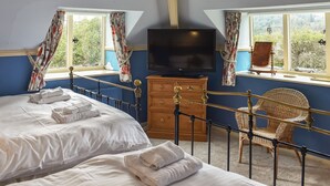 A hotel room with two beds, a television, a wooden dresser, and a wicker chair. - 2 bedroom accommodation in Sawrey, near Ambleside (Sawrey, near Ambleside)