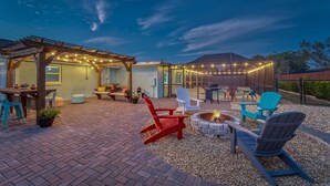 Ein Außenbereich mit Terrassenausstattung, einem Feuerkorb, Adirondack-Stühlen und einer Pergola mit Lichterkette.