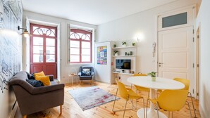 A modern living room with a grey sofa, yellow chairs, a white table, and wooden flooring. - VIVA Trindade Downtown (Porto)