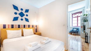 A modern hotel room with a large bed, a geometric wall art piece, and a view into the living area. - VIVA Trindade Downtown (Porto)