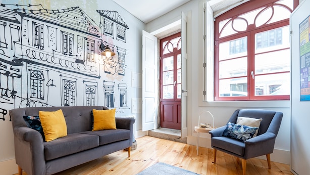 A living room with a grey sofa, a blue armchair, wooden flooring, a red door, and a wall mural. - VIVA Trindade Downtown (Porto)