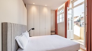 A modern bedroom with a large bed, a wardrobe, and a balcony with curtains.
