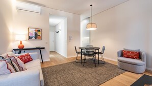 A modern living room with a sofa, a dining table with chairs, a small armchair, a lamp, and a rug.