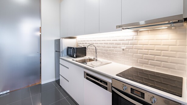 A modern kitchen with white cabinetry, a stainless steel sink, a microwave, and a built-in oven.