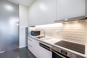 A modern kitchen with white cabinetry, a stainless steel sink, a microwave, and a built-in oven. - VIVA SIZE Flat Batalha - Apartment 4 (Porto)