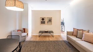 A modern living room with a sofa, a dining table, and a coffee table. There are two framed artworks on the wall.