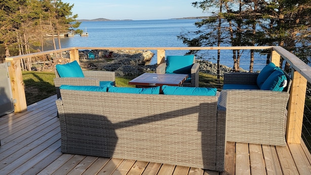 Un terrazzino in legno con mobili in vimini e vista sull'acqua.