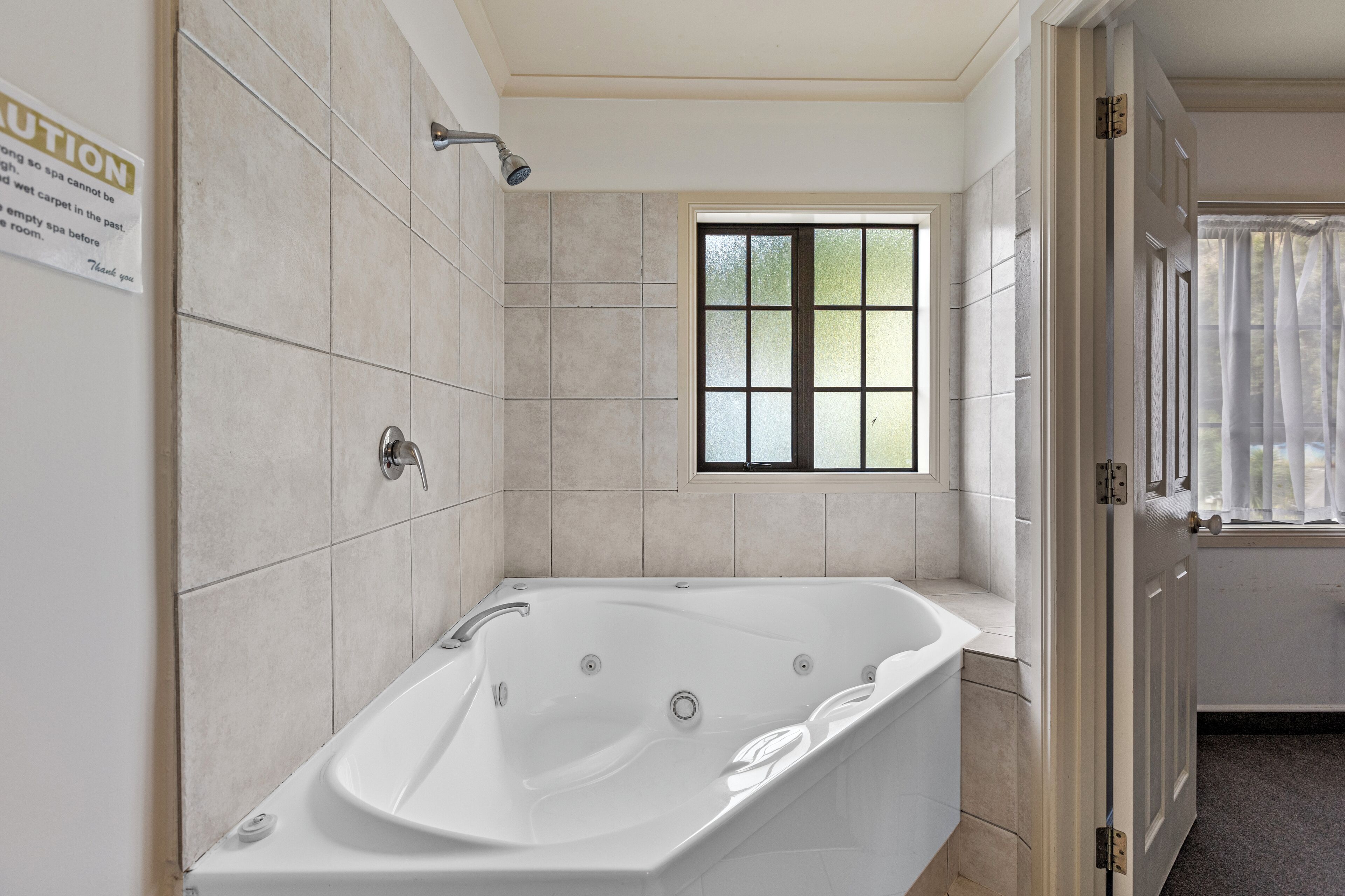 A bathroom with a large bathtub, a showerhead, and a window providing natural light.