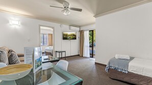 Habitación de hotel con cama, escritorio con silla, ventilador de techo, televisor y vistas al exterior.