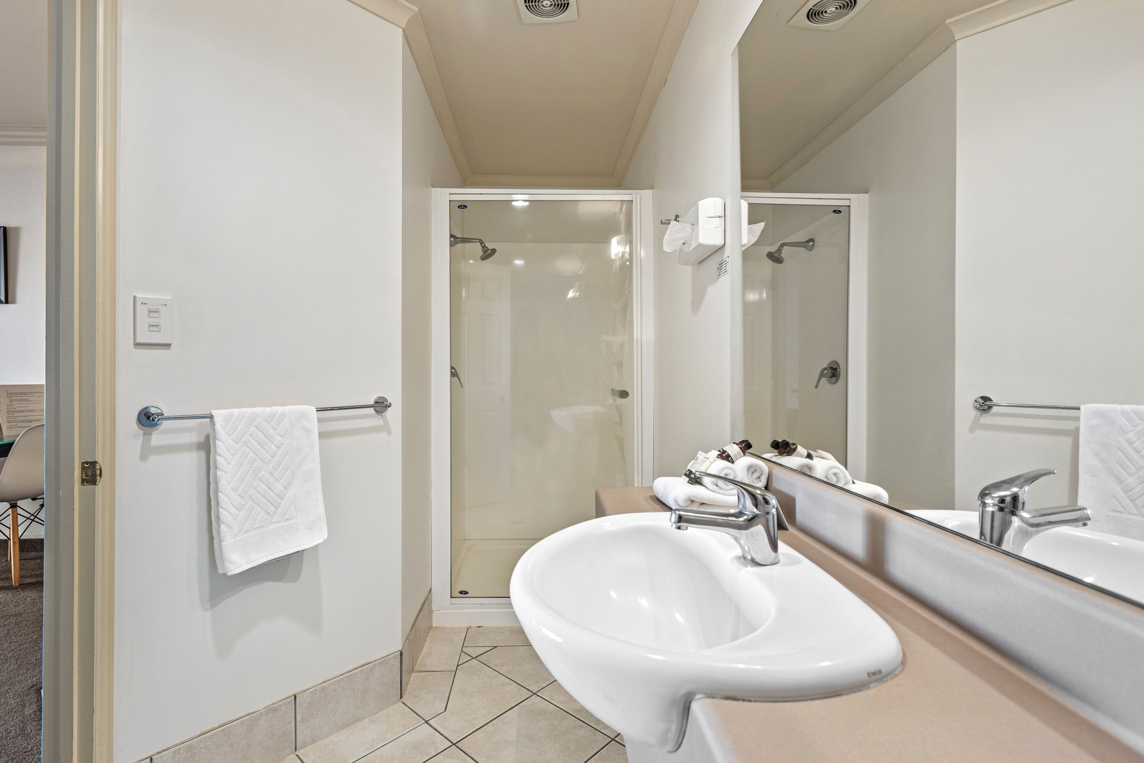 A modern bathroom with a glass-enclosed shower, a large mirror, and a white sink.