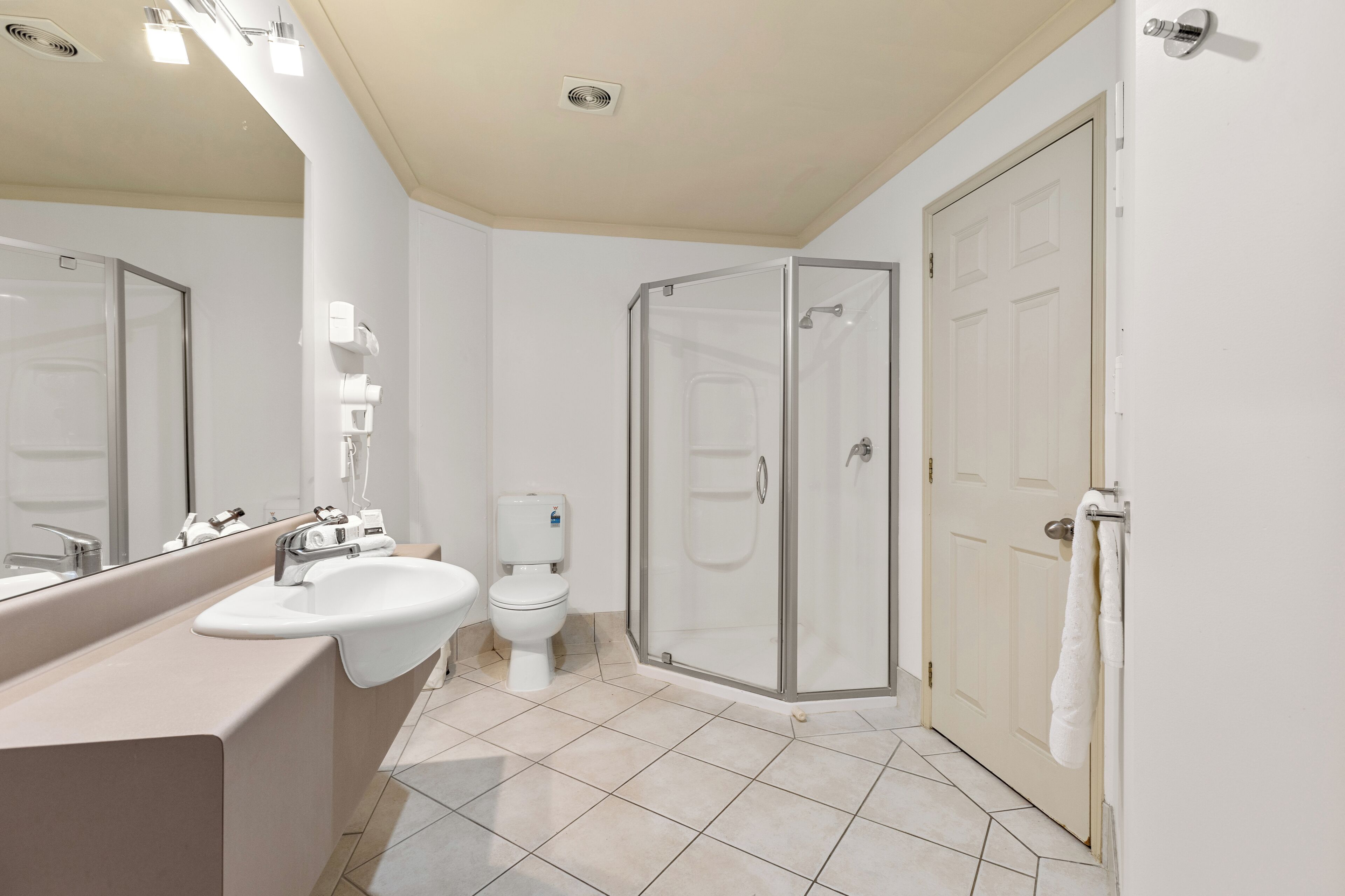 Un baño moderno con un espejo grande, un lavamanos, un inodoro y una ducha con mampara de vidrio.