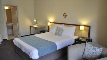 A hotel room with a large bed, bedside tables with lamps, a sofa, and a bathroom visible through an open door.