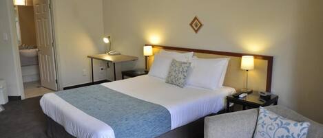 A hotel room with a large bed, bedside tables with lamps, a sofa, and a bathroom visible through an open door.