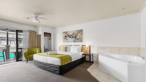 Una habitación de hotel con cama, un sillón verde, una bañera y un balcón con vistas.