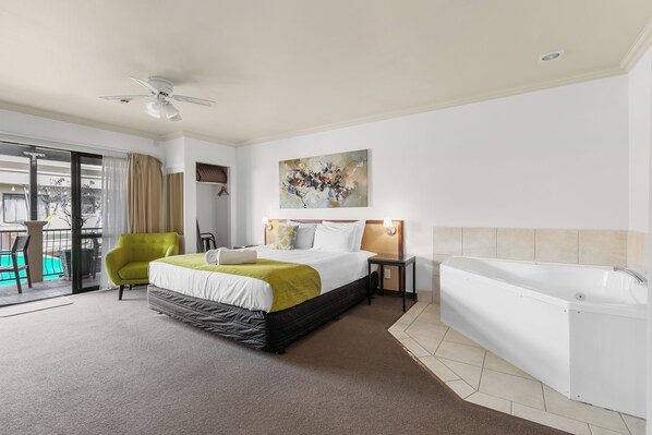 A hotel room with a bed, a green armchair, a bathtub, and a balcony with a view.