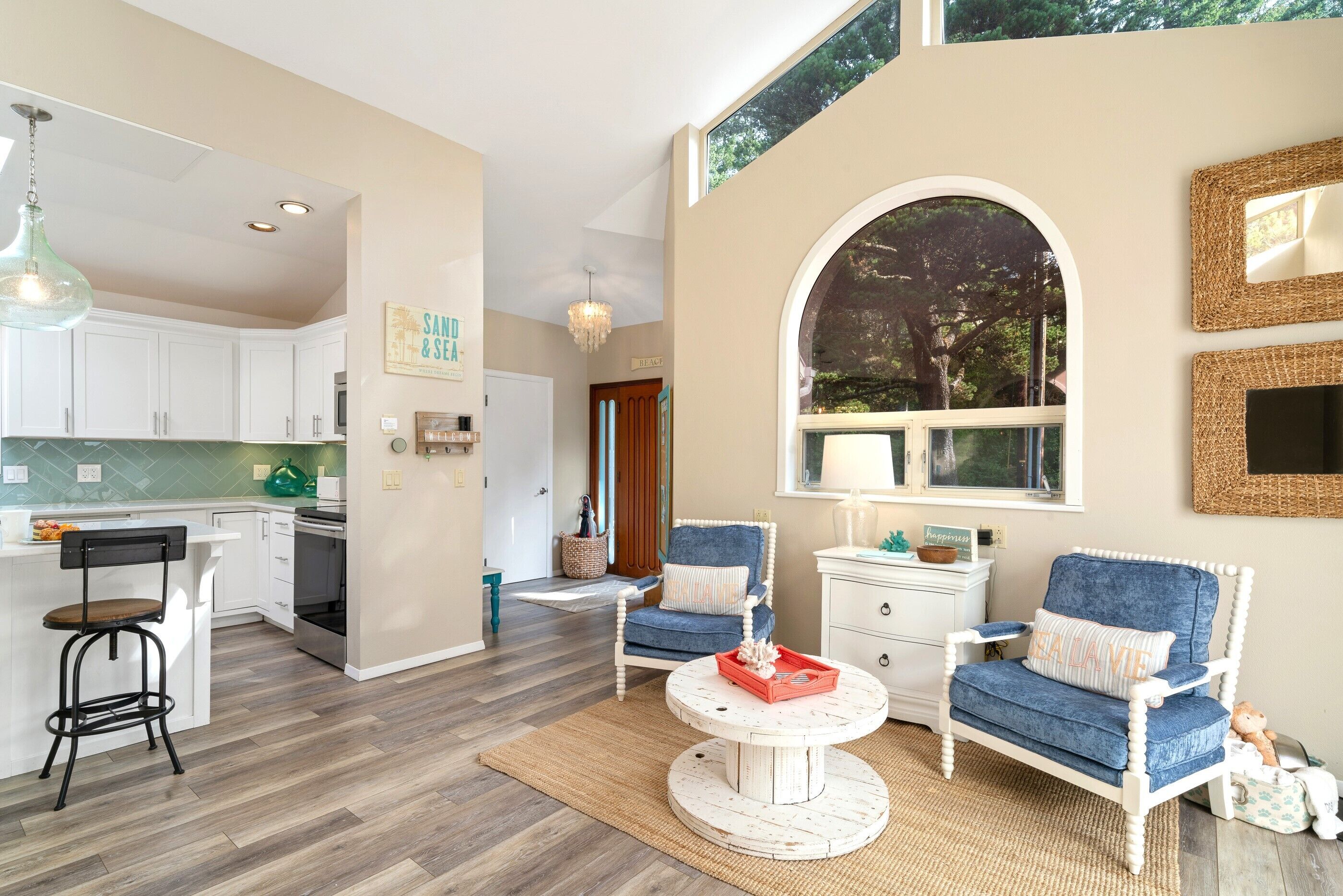 A spacious living area with a kitchen, a round coffee table, and two blue armchairs.