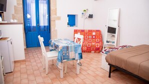 Een kleine kamer met een eettafel, stoelen, een bed en een kleine kitchenette.