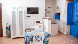 Een compacte kamer met kitchenette, een eethoek met tafel en stoelen, een televisie en een blauwe deur.