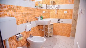 Een badkamer met toilet, bidet en wastafel, met oranje en witte betegelde wanden en witte vloertegels.