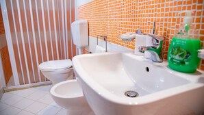Een badkamer met een wit toilet, een witte wastafel en een zeepdispenser.