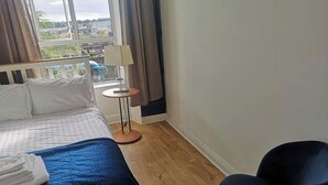 A hotel room with a bed, a chair, a small table, and a view of the outside. - Perfect Apartment - Close to the Train Station (Cork)
