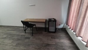 A room with a wooden desk, a black chair, a small black cabinet, and a radiator with curtains. - Cozy Airport Guesthouse - Woolway Studios (Argavand,)