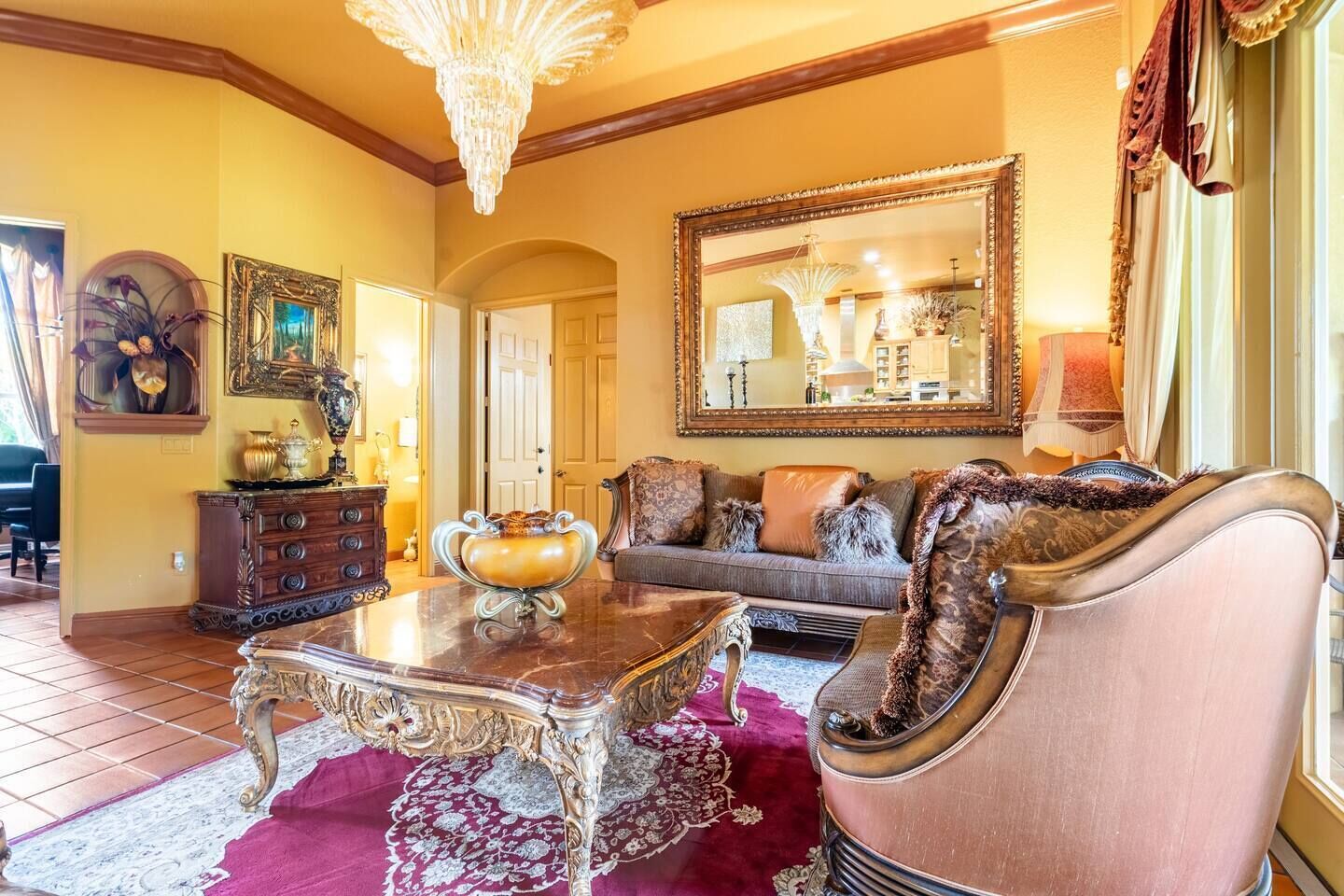 A spacious living room with a large chandelier, a grand mirror, and a plush sofa.