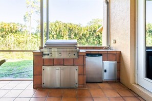 An outdoor kitchen with a grill, a built-in sink, and a dishwasher, set against a backdrop of greenery. - Near Lion Country Safari! Large Family-sized home (Loxahatchee)
