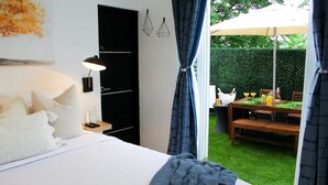 Een slaapkamer met een bed, nachtkastje, lamp en uitzicht op een buiten eethoek met een tafel en stoelen.