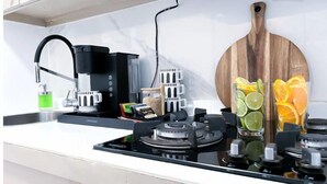 Een keuken met een zwarte koffiezetapparaat, een wit aanrecht, een houten snijplank en twee glazen met fruit.