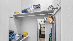 A narrow hallway with storage shelves on either side, holding folded towels and a few personal items. - Perfect Urban Escape: Your Personal Oasis with a Zen Den and Lush Gardens! (Delray Beach)