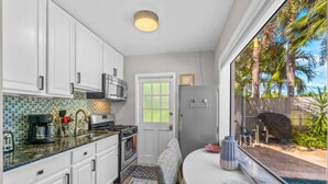A compact kitchen with white cabinets, a built-in microwave, and a coffee maker. There's a dining area with a table and chairs, and a view of a swimming pool outside. - Perfect Urban Escape: Your Personal Oasis with a Zen Den and Lush Gardens! (Delray Beach)