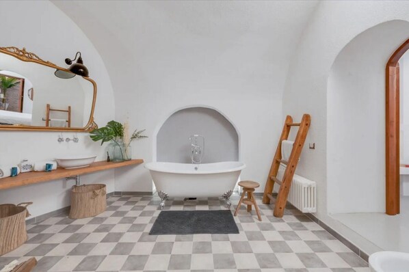 Ein Badezimmer mit einer freistehenden Badewanne, einem Holzbadezimmer-Möbelkorpus, einem Spiegel und einem Heizkörper.