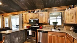 A kitchen with wooden cabinets, stainless steel appliances, and a granite countertop. - Old Mill Cabin #1 - on the Little MO River, large yard, close to Diamond Mine! (Murfreesboro)