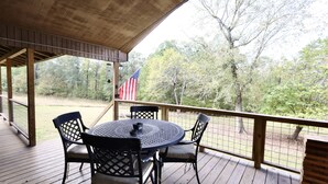 A covered outdoor deck with a round table and chairs, an American flag, and a view of trees. - Old Mill Cabin #1 - on the Little MO River, large yard, close to Diamond Mine! (Murfreesboro)
