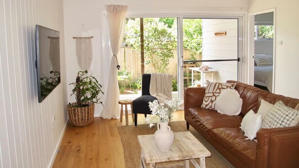 A living room with a brown leather sofa, a small wooden coffee table, a wicker basket, and a potted plant. - WERRI North.
 (Werri Beach)