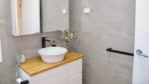 A modern bathroom with a large mirror, a white sink, and a wooden countertop. - WERRI North.
 (Werri Beach)