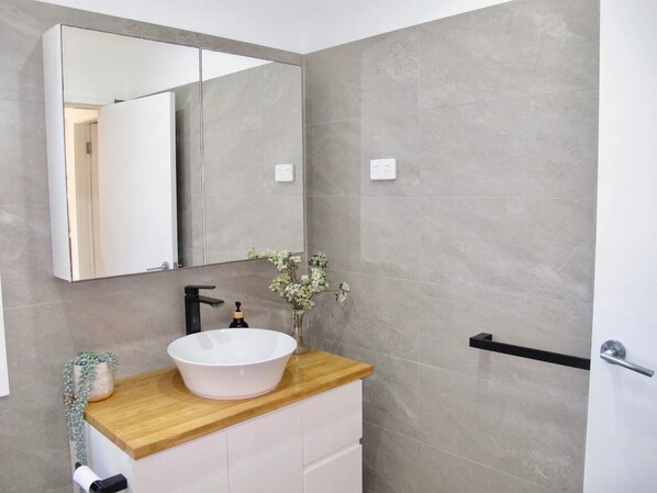A modern bathroom with a large mirror, a white sink, and a wooden countertop. - WERRI North. (Werri Beach)