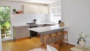 A modern kitchen with white cabinets, a large island with stools, and a dining area with a table and chairs. - WERRI North.
 (Werri Beach)