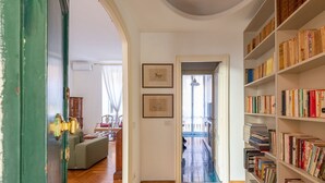 Un pasillo con suelo de madera, una puerta verde, una estantería llena de libros y un cuadro en la pared.