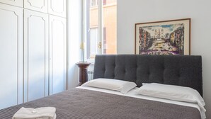 Un dormitorio con cama, ventana, un cuadro y un armario blanco.